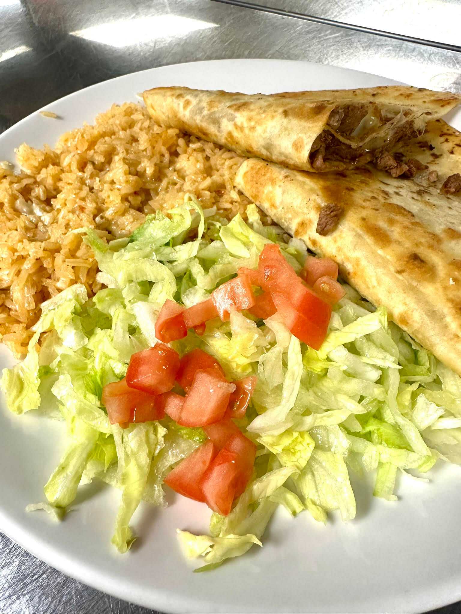 Plate with quesadillas, Spanish rice, and a side salad topped with diced tomatoes on a white plate.