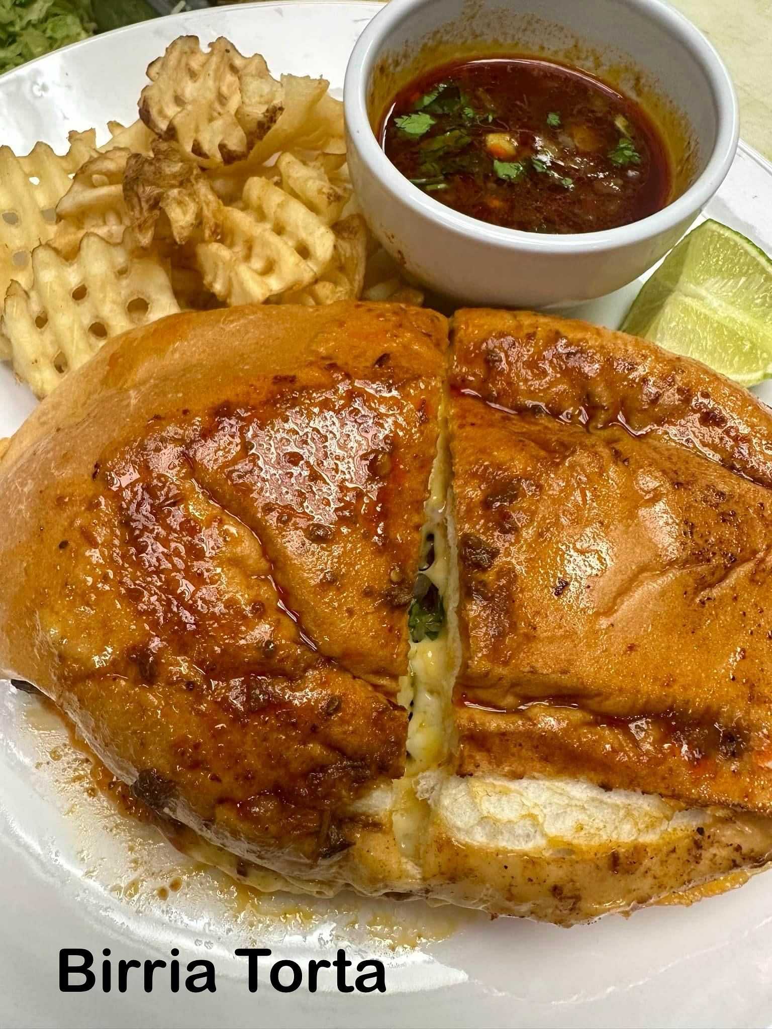 Birria Torta with waffle fries and a dipping sauce on a white plate.