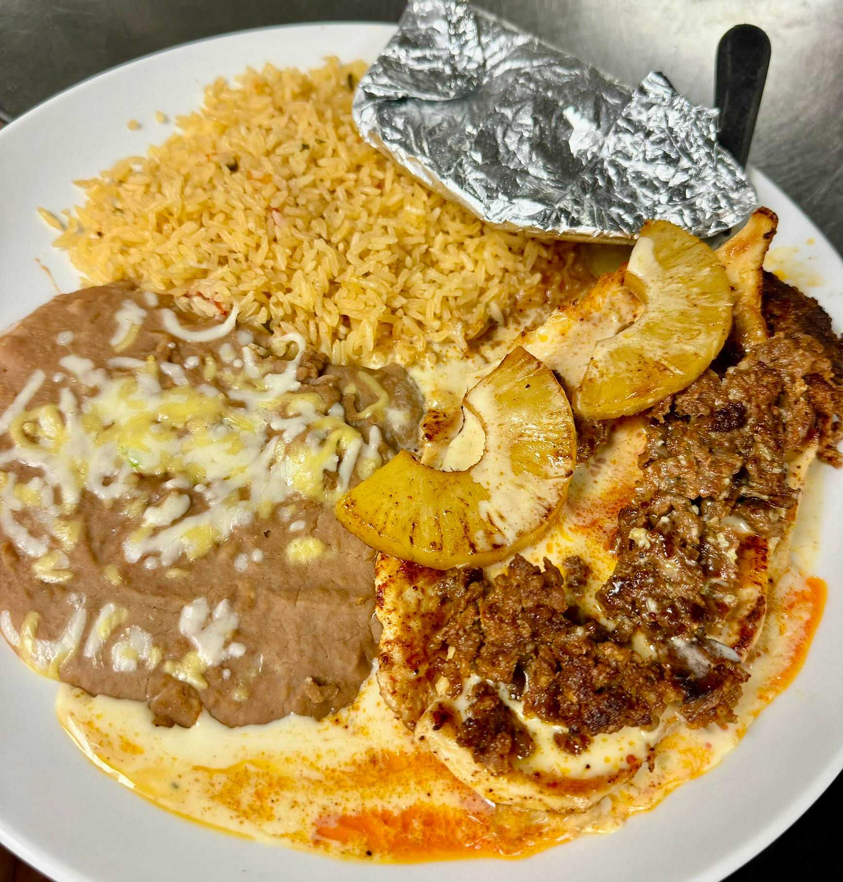 Grilled chicken with pineapples, refried beans with cheese, and rice on a white plate.